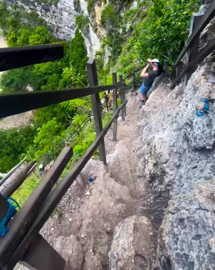 Narrow hiking path along the cliff of KelingKing Beach with only a wooden fence to keep hikers from falling