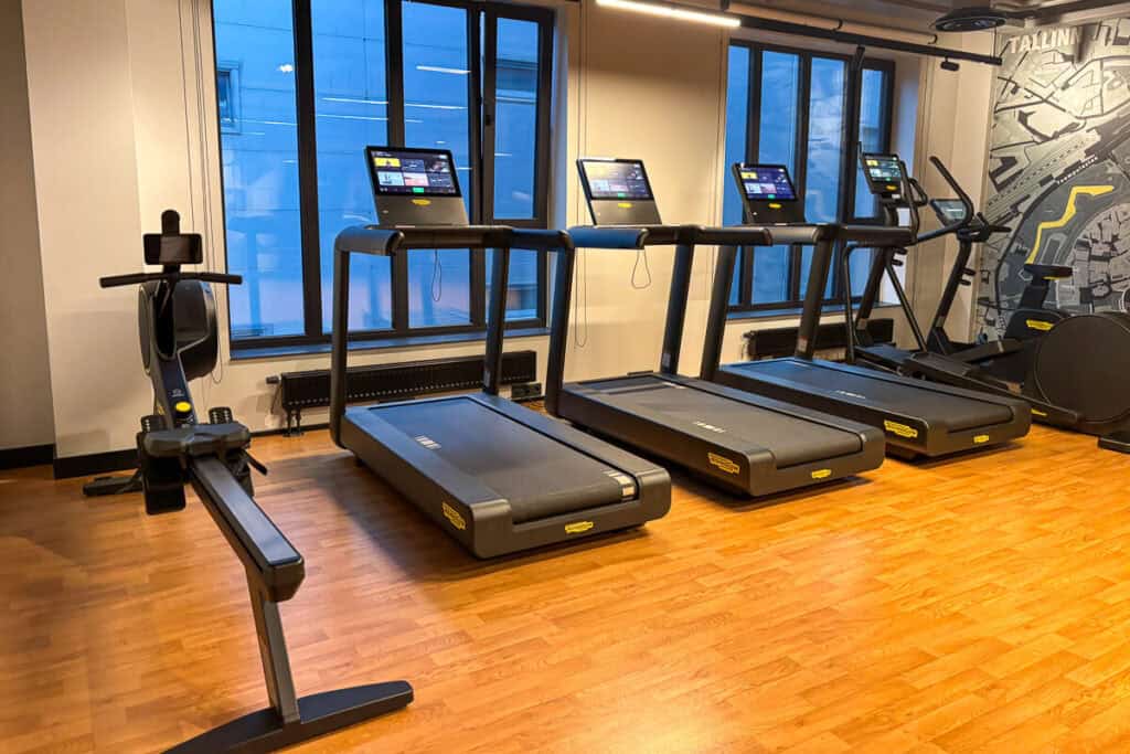 Cardio section of the fitness center at Hyatt Place Tallinn with treadmills, a rowing machine, and large windows overlooking the city, set against a modern map-themed accent wall.