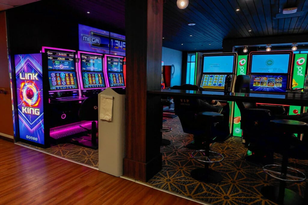 Onboard casino area on a Tallinn to Helsinki ferry, featuring brightly lit slot machines including “Link King” and “Paf” games. The space has dim lighting, bar stools, and a patterned carpet for a lounge-like atmosphere.