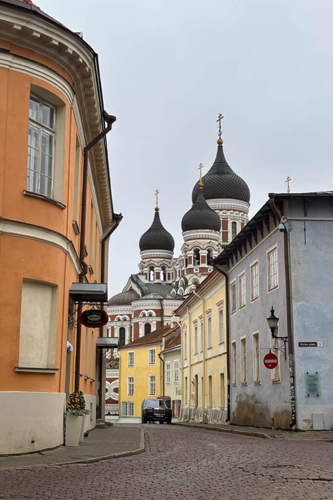 Pastel buildings line a quiet cobblestone street leading to Alexander Nevsky Cathedral with its onion domes rising in the background, a striking stop during one day in Tallinn.