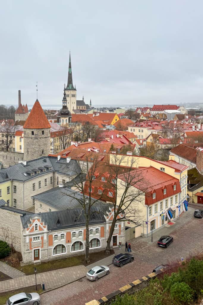 View over Tallinn Old Town with red tiled rooftops, historic towers, and St Olaf’s Church rising above the skyline on a cloudy day, a scenic highlight when spending one day in Tallinn.