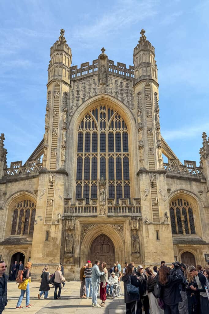 Front view of Bath Abbey’s ornate stone facade with tall gothic windows and carved details as a crowd gathers in the square below, a popular stop on a 2 day Bristol and Bath itinerary from London.