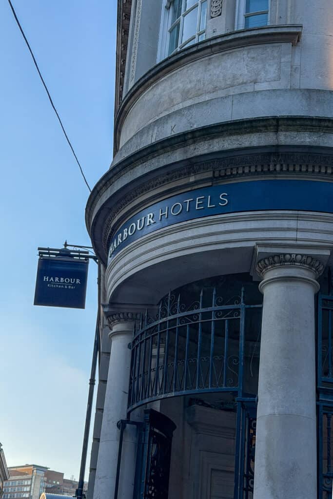 Curved stone building entrance with columns and signage reading “HARBOUR HOTELS” and “Harbour Kitchen & Bar” in Bristol, highlighting a stylish place to stay on a 2 day Bristol and Bath itinerary from London.