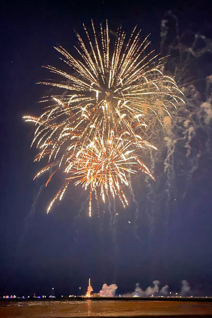 Two large firework bursts light up the night sky over the water in Key West, with smoke trails drifting below.