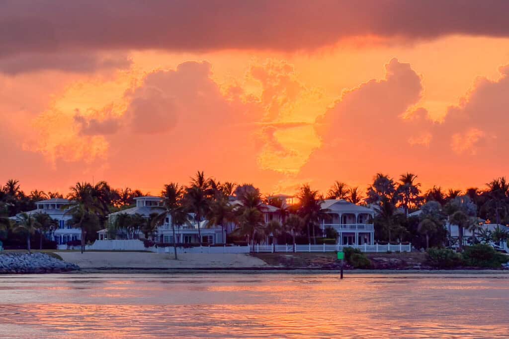 A vivid orange and pink sunset over the water with palm trees and waterfront homes on Sunset Key in Key West.